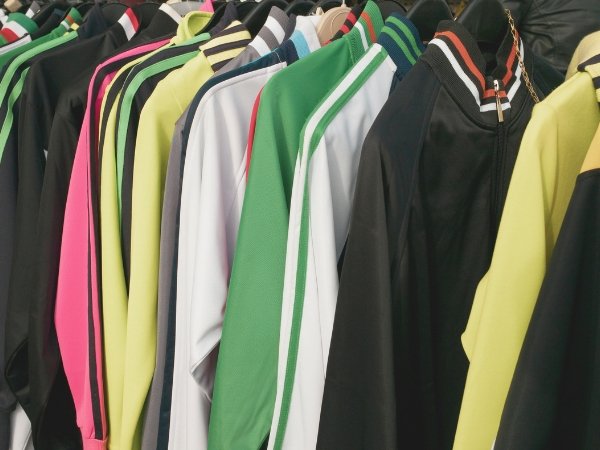 Row of colorful track jackets hanging on a rack, featuring black, pink, yellow, gray, green, and white with striped sleeves